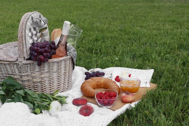 Photo of Picnic blanket with tasty food, flowers, basket and cider on green grass outdoors