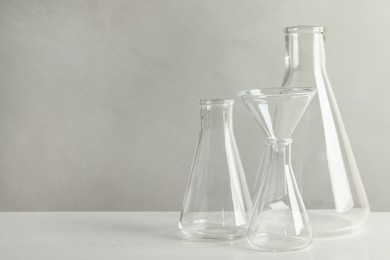Set of laboratory glassware on white table against grey background, space for text