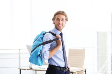 Young handsome businessman holding fitness bag in office. Gym after work