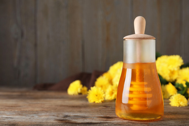 Photo of Jar with organic honey and chrysanthemum flowers on wooden table. Space for text
