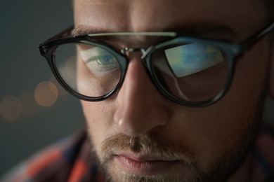 Young man wearing glasses on blurred background, closeup. Ophthalmology service