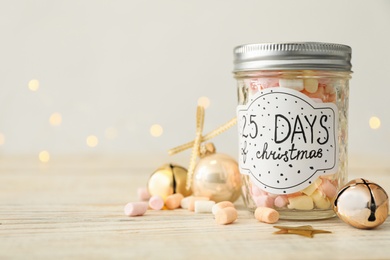 Glass jar with label 25 Days of Christmas and tasty marshmallows on white wooden table against blurred background, space for text. Advent calendar