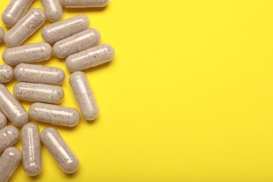 Many gelatin capsules on yellow background, flat lay. Space for text