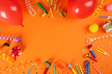 Frame of colorful serpentine streamers and other party accessories on orange background, flat lay. Space for text