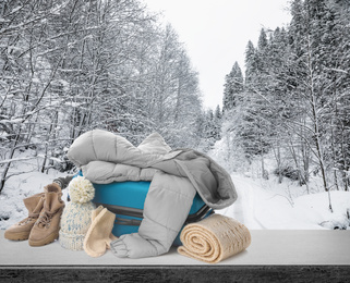 Suitcase with warm clothes on stone surface against beautiful winter landscape