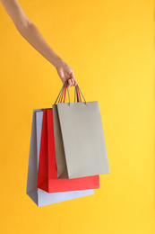 Woman with paper shopping bags on yellow background, closeup