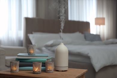 Aroma oil diffuser, candles and books on wooden table in bedroom