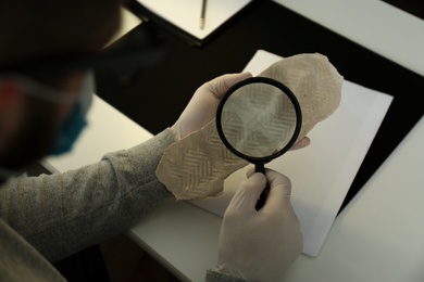 Detective with magnifying glass examining shoe sole print at table, closeup