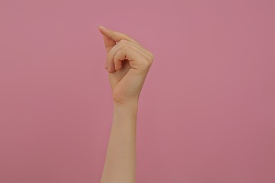 Woman showing thumb and index finger together on pink background, closeup