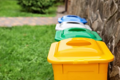 Photo of Many colorful recycling bins near stone wall outdoors, closeup. Space for text