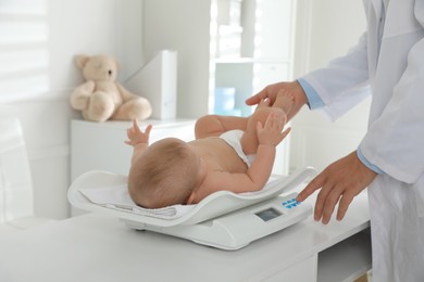 Pediatrician weighting cute baby in clinic, closeup. Health care