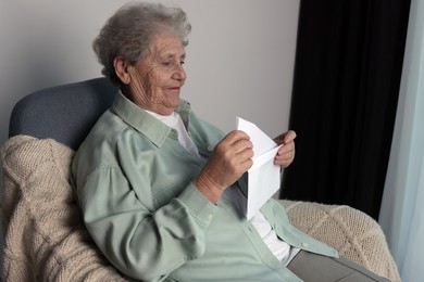 Elderly woman with letter in armchair indoors. Loneliness concept