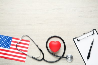 Stethoscope, red heart, clipboard and American flag on white wooden table, flat lay. Space for text
