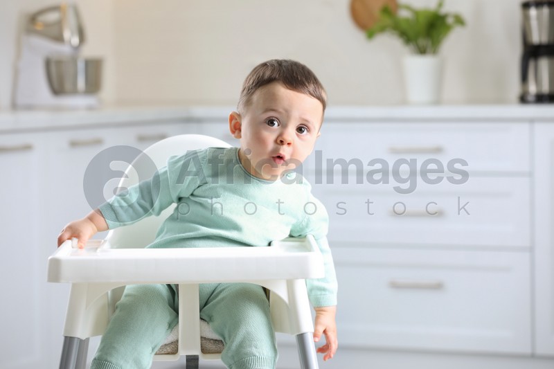 Cute little baby sitting in high chair at kitchen. Space for text