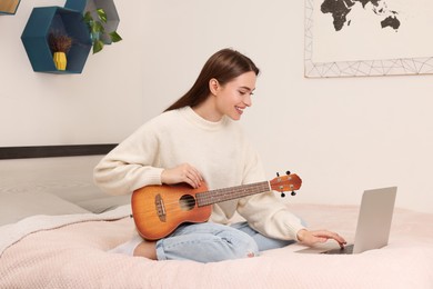 Happy young woman learning to play ukulele with online music course at home. Time for hobby