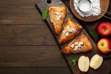 Photo of Fresh tasty puff pastry with sugar powder, mint and apples served on wooden table, flat lay. Space for text