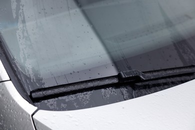 Photo of Wiper cleaning raindrops from car windshield, closeup