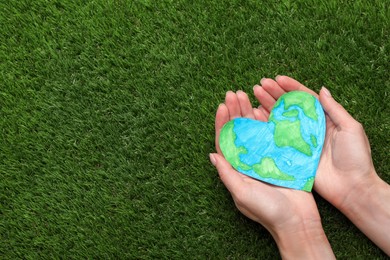 Happy Earth Day. Woman with heart shaped plasticine planet on green grass, top view and space for text