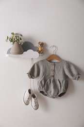 Cute baby onesie and shoes hanging on white wall