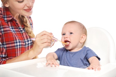 Woman feeding her child in highchair against white background. Healthy baby food