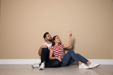 Young couple sitting on floor near beige wall indoors