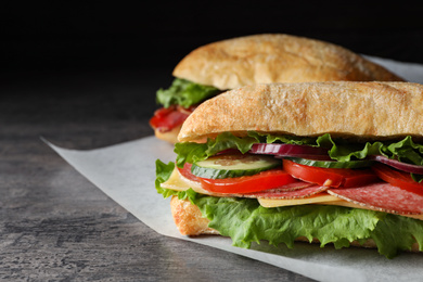 Photo of Delicious sandwiches with fresh vegetables and salami on grey table, closeup