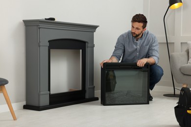 Man installing electric fireplace near wall in room