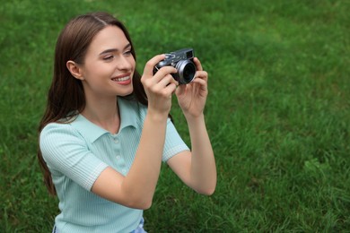 Photo of Young woman with camera taking photo on green grass outdoors, space for text. Interesting hobby