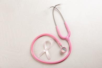 Pink ribbon and stethoscope on light grey stone background, flat lay. Breast cancer concept