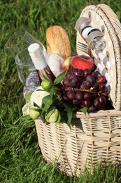 Picnic basket with tasty food, flowers and cider on grass