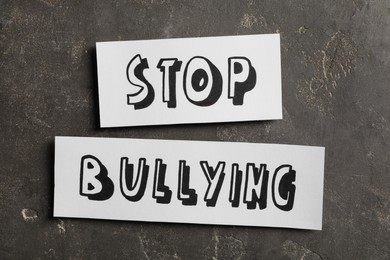 Pieces of paper with text Stop Bullying on grey stone surface, flat lay