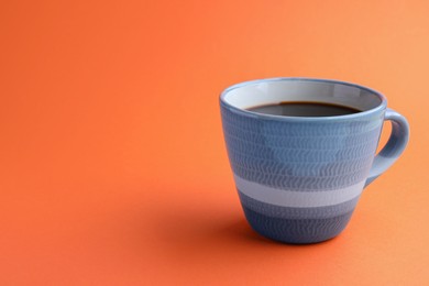 Photo of Grey mug of freshly brewed hot coffee on orange background, space for text
