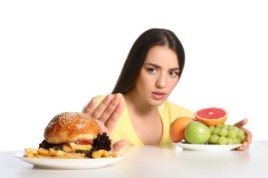 Woman choosing between fruits and burger with French fries on white background