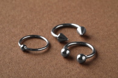 Photo of Stylish captive bead and horseshoe rings on brown background, closeup. Piercing jewelry