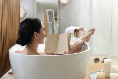 Beautiful young woman reading book while taking bath at home