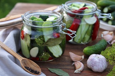 Photo of Glass jars with fresh cucumbers and other ingredients on wooden table, closeup. Canning vegetables