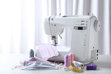 Photo of Sewing machine, homemade protective masks and craft accessories on table