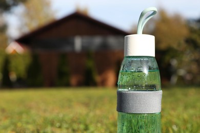 Photo of Glass bottle of fresh water on green grass outdoors. Space for text