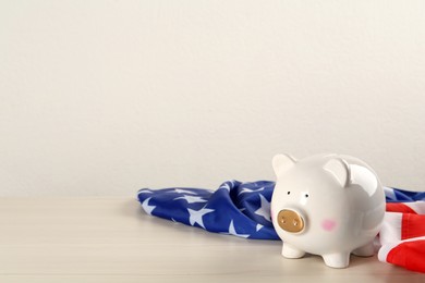 Photo of Piggy bank and American flag on white wooden table, space for text