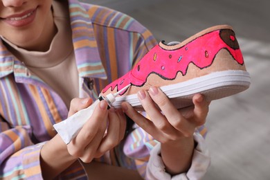 Photo of Woman painting on sneaker indoors, closeup. Customized shoes