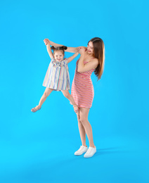 Young mother and little daughter having fun on light blue background