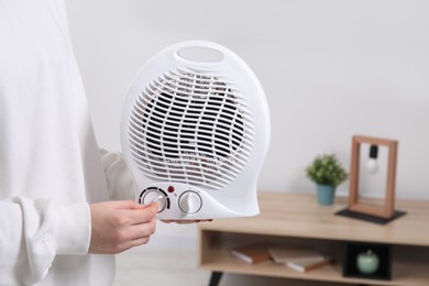 Photo of Woman turning on electric fan heater at home, closeup. Space for text