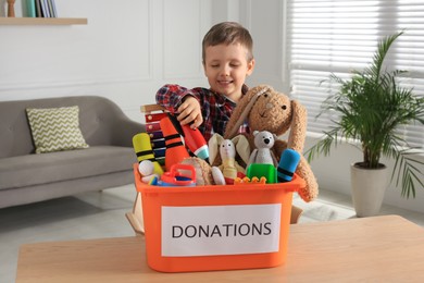 Cute little boy putting toy into donation box at home
