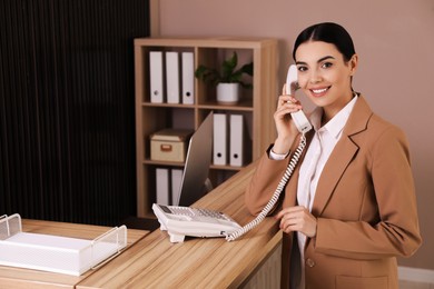 Receptionist talking on phone near countertop in office, space for text