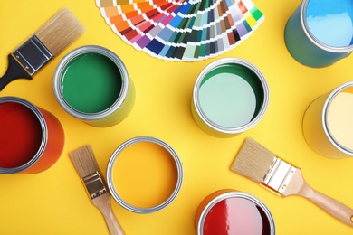 Flat lay composition with paint cans, brushes and color palette on yellow background