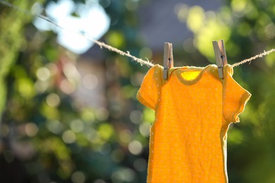 Photo of Baby bodysuit drying on washing line against blurred background, closeup