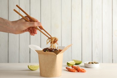 Woman eating seafood wok noodles with chopsticks from box at white wooden table, closeup. Space for text