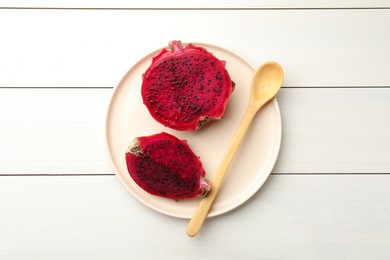 Plate with delicious cut red pitahaya fruit and spoon on white wooden table, top view