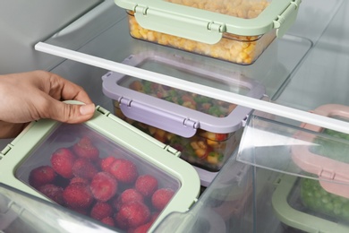 Photo of Woman taking box with frozen strawberry from refrigerator, closeup
