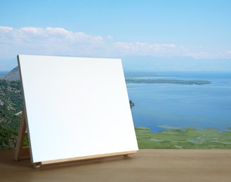 Wooden easel with blank canvas on table and beautiful seascape. Space for text
